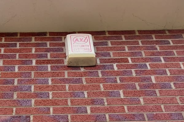 Shown is an old AXL security systems intruder alarm bell-box, faded due to age.